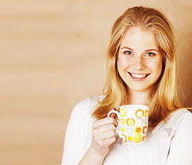 Image showing young cute blond girl drinking coffee close up on warm brown bac