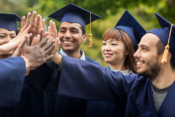 Image showing happy students in mortar boards making high five