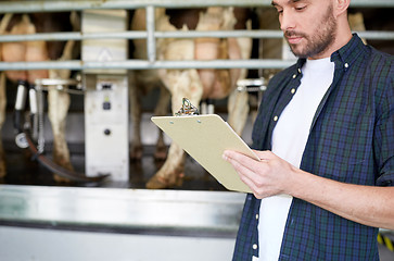 Image showing young man with clipboard and cows on dairy farm