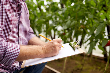 Image showing senior man writing to clipboard at farm greenhouse