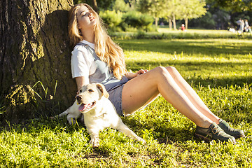 Image showing young attractive blond woman playing with her dog in green park at summer, lifestyle people concept