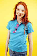 Image showing young pretty red hair teenage hipster girl posing in glasses emotional happy smiling on yellow background, lifestyle people concept 