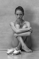 Image showing Tired ballet dancer sitting on the wooden floor on a pink background