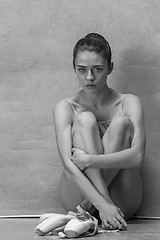 Image showing Tired ballet dancer sitting on the wooden floor on a pink background