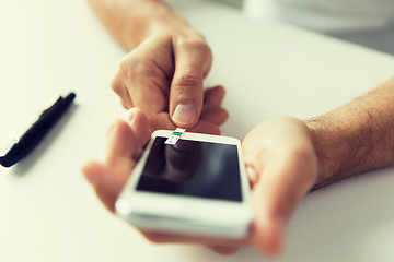 Image showing close up of man with smartphone making blood test