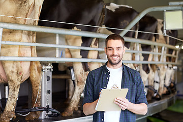 Image showing man with clipboard and milking cows on dairy farm