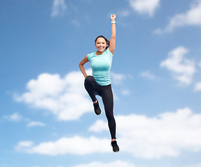 Image showing happy smiling sporty young woman jumping in air