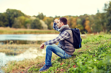 Image showing smiling man with backpack resting on river bank