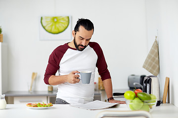Image showing man reading newspaper and eating at home kitchen
