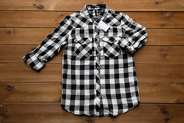 Image showing checkered shirt with tag on wooden background