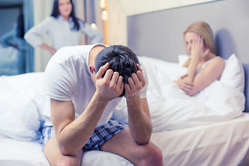 Image showing man sitting on the bed with two women on the back