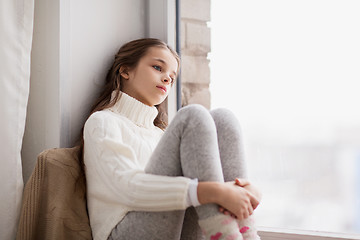 Image showing sad girl sitting on sill at home window in winter