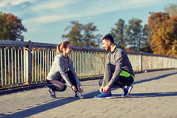 Image showing smiling couple tying shoelaces outdoors