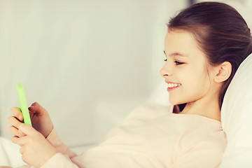 Image showing happy girl lying in bed with smartphone at home