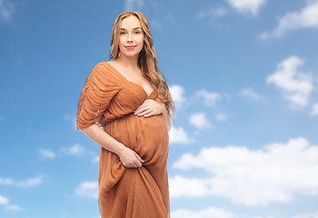 Image showing happy pregnant woman touching her belly over sky