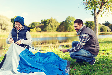 Image showing happy father and son setting up tent outdoors