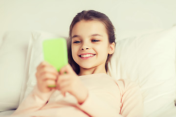 Image showing happy girl lying in bed with smartphone at home