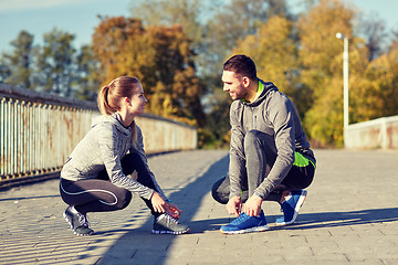 Image showing smiling couple tying shoelaces outdoors