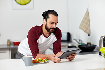 Image showing man with tablet pc eating at home kitchen