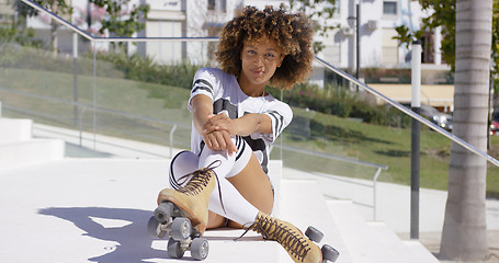 Image showing Smiling female sitting on stairs wearing rollerskates