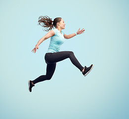 Image showing happy smiling sporty young woman jumping in air