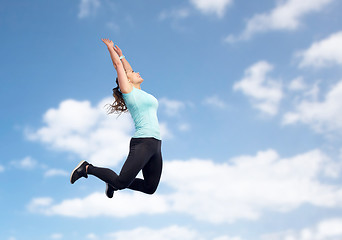 Image showing happy sporty young woman jumping in blue sky