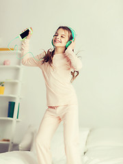 Image showing girl jumping on bed with smartphone and headphones