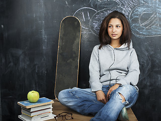 Image showing young cute teenage girl in classroom at blackboard seating on table smiling, modern hipster concept