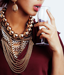 Image showing young african-american woman drinking champagne, holding glass, wearing lot of golden jewelry 