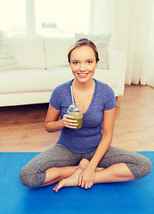 Image showing happy woman with smoothie sitting on mat at home