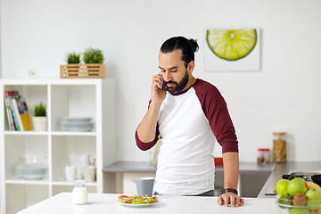 Image showing man calling on smartphone and eating at home