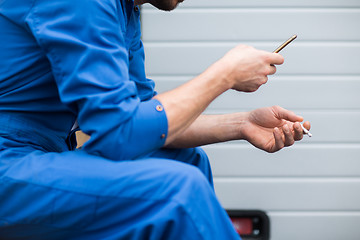 Image showing auto mechanic smoking cigarette at car workshop