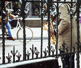 Image showing african street musician playing jazz on saxophone throw lattice 