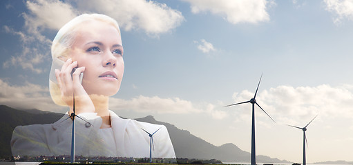 Image showing businesswoman with smartphone over wind turbines