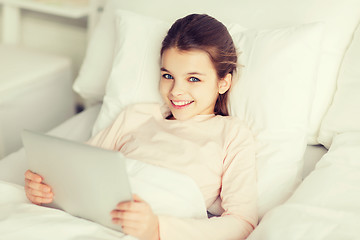 Image showing happy girl lying in bed with tablet pc at home