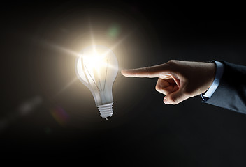 Image showing businessman pointing finger to lightbulb over dark