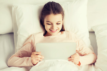 Image showing happy girl lying in bed with tablet pc at home