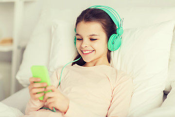 Image showing happy girl lying in bed with smartphone at home