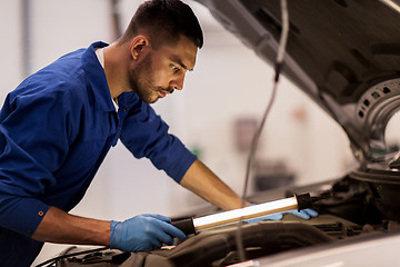 Image showing mechanic man with lamp repairing car at workshop