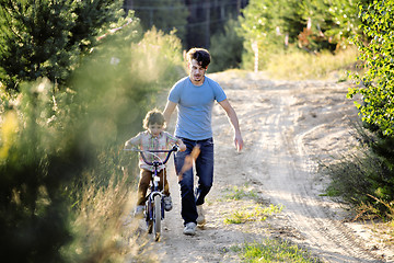 Image showing father learning his son to ride on bicycle outside, real happy family in summer forest enjoing nature