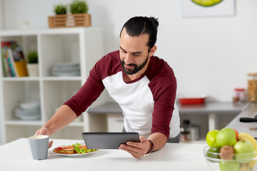 Image showing man with tablet pc eating at home kitchen