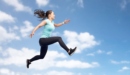 Image showing happy sporty young woman jumping in blue sky