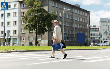 Image showing senior man with shopping bags walking on crosswalk