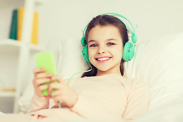 Image showing happy girl lying in bed with smartphone at home