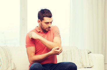 Image showing unhappy man suffering from pain in hand at home