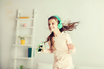 Image showing girl jumping on bed with smartphone and headphones