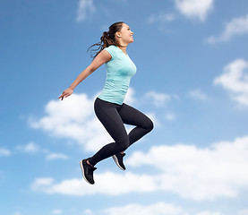 Image showing happy smiling sporty young woman jumping in sky