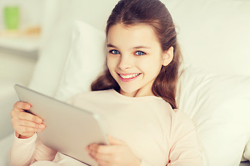 Image showing happy girl lying in bed with tablet pc at home