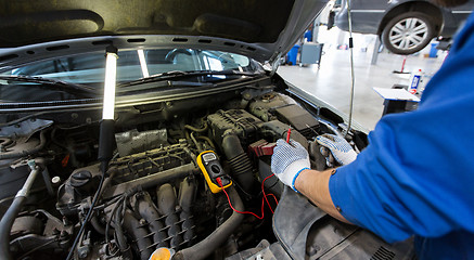 Image showing auto mechanic man with multimeter testing battery