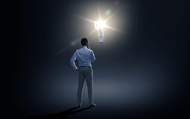 Image showing businessman looking at lighting bulb over dark